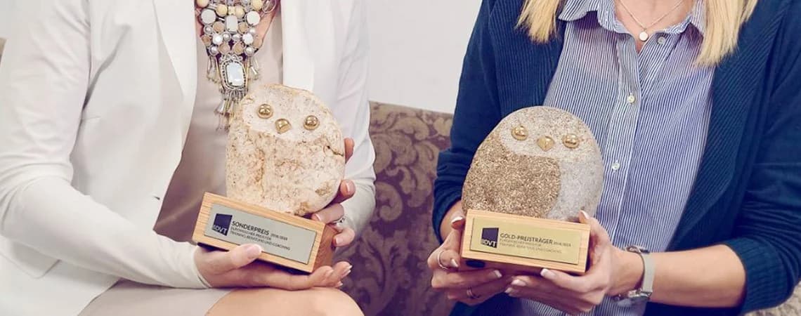 Zwei BDVT-Trophäen in Eulenform mit den Schildern „Sonderpreis“ und „Gold-Preisträger“, gehalten von Eva-Maria Kraus und einer Kollegin