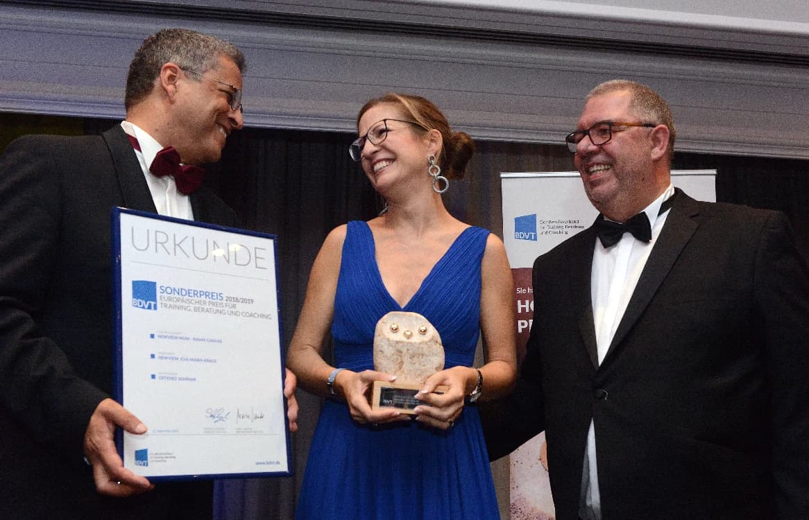 Eva-Maria Kraus nimmt den BDVT-Sonderpreis 2018/2019 entgegen und hält die Trophäe in Eulenform, daneben zwei Laudatoren mit der Urkunde